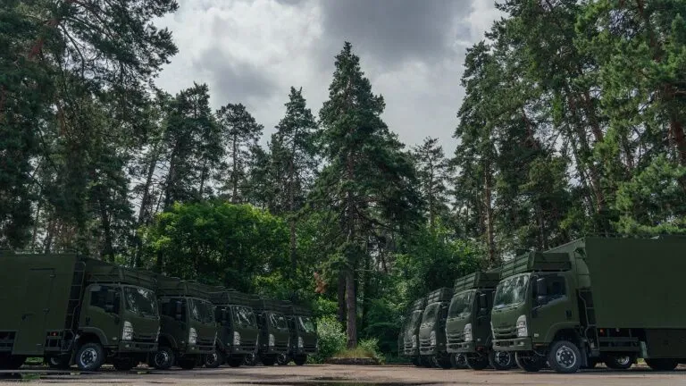 Колона військових вантажівок у сосновому лісі